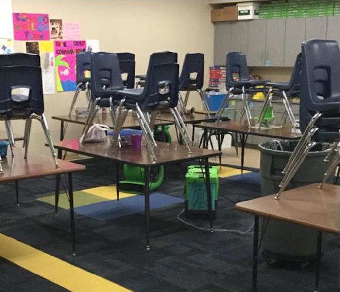 Classroom with SERVPRO equipment on the floor and chairs stacked on tables 