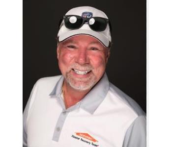 male smiling, wearing white logo'd shirt with white cap and sunglasses resting on cap