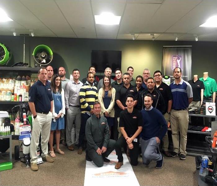 A large group of people in a room with SERVPRO equipment 