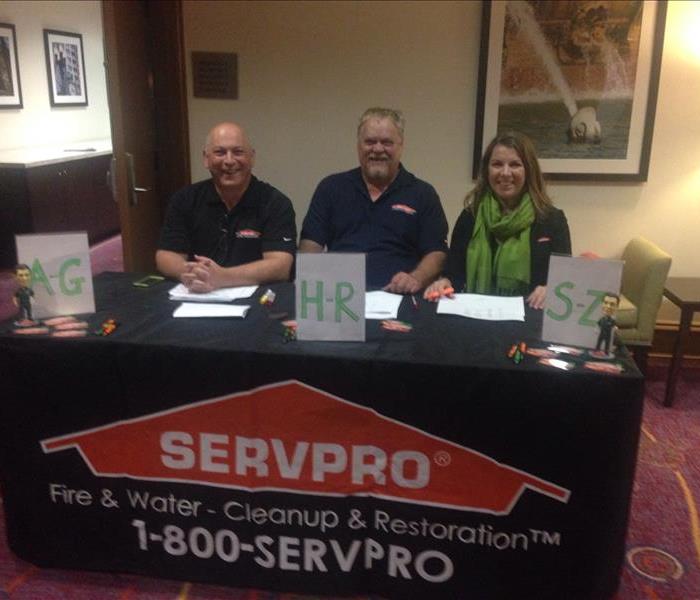 Three people sitting at a table with a SERVPRO banner covering the table