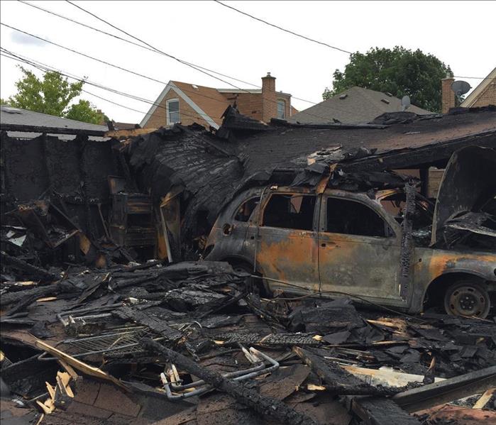 The exterior of home with severe fire damage by charred vehicle