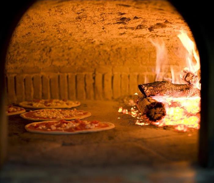A clay oven with pizzas cooking next to a fire